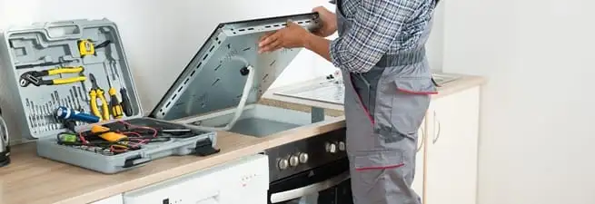 Cooktop repair technician lifting a built-in stovetop for service in San Antonio, TX
