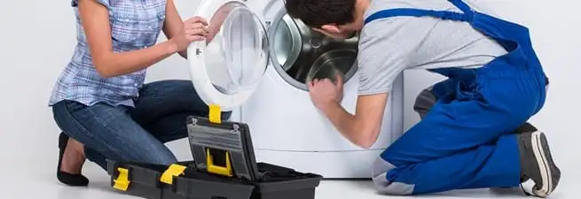 Washer repair technician inspecting a front-load washing machine with tools in San Antonio, TX