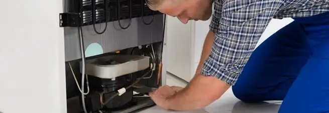 Refrigerator repair technician servicing the compressor and condenser area in San Antonio, TX