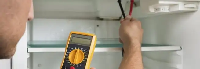 Refrigerator repair technician testing electrical components with a multimeter in San Antonio, TX