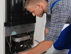 Refrigerator repair technician servicing the compressor and condenser area in San Antonio, TX